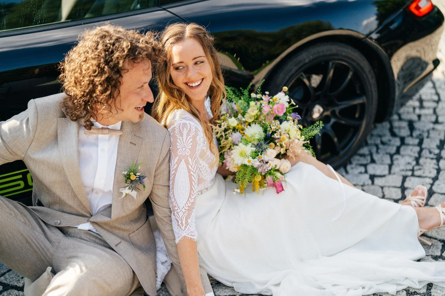 Anička a Norbert sedí na dlažbě opření o černé Porsche