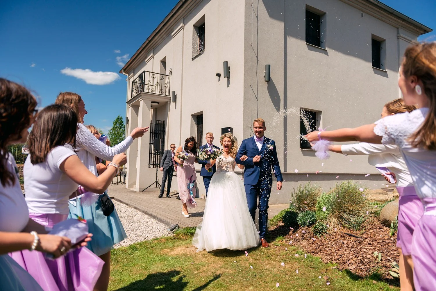 Novomanželé odcházejí mezi gratulujícími hosty.