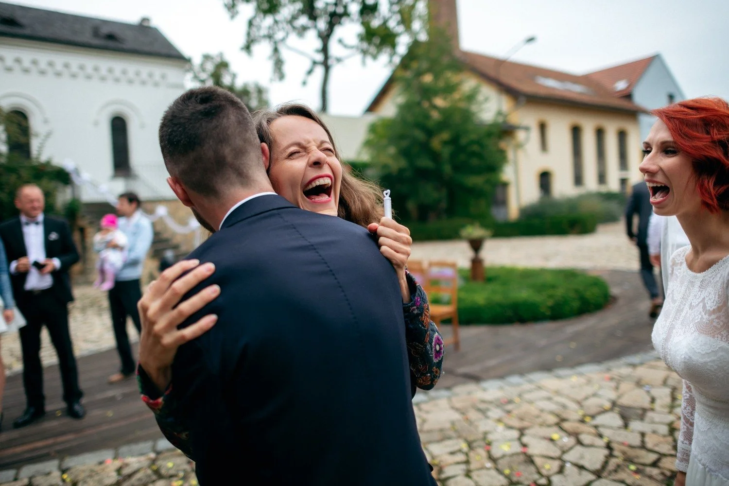 Lukáš objímá smějící se ženu na dlážděném nádvoří.