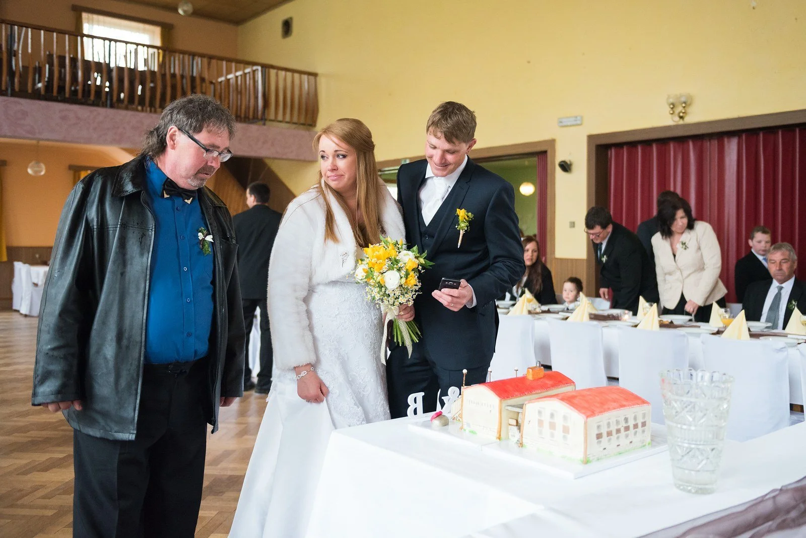 Nevěsta a ženich si prohlížejí svatební dort ve tvaru budovy na prostřeném stole.