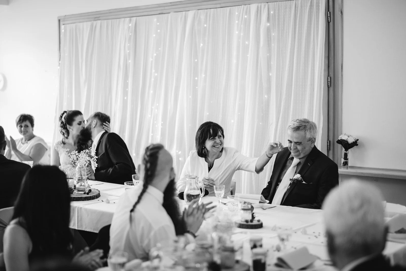 Černobílá fotografie ukazuje řadu hostů sedících vedle sebe u slavnostního stolu.