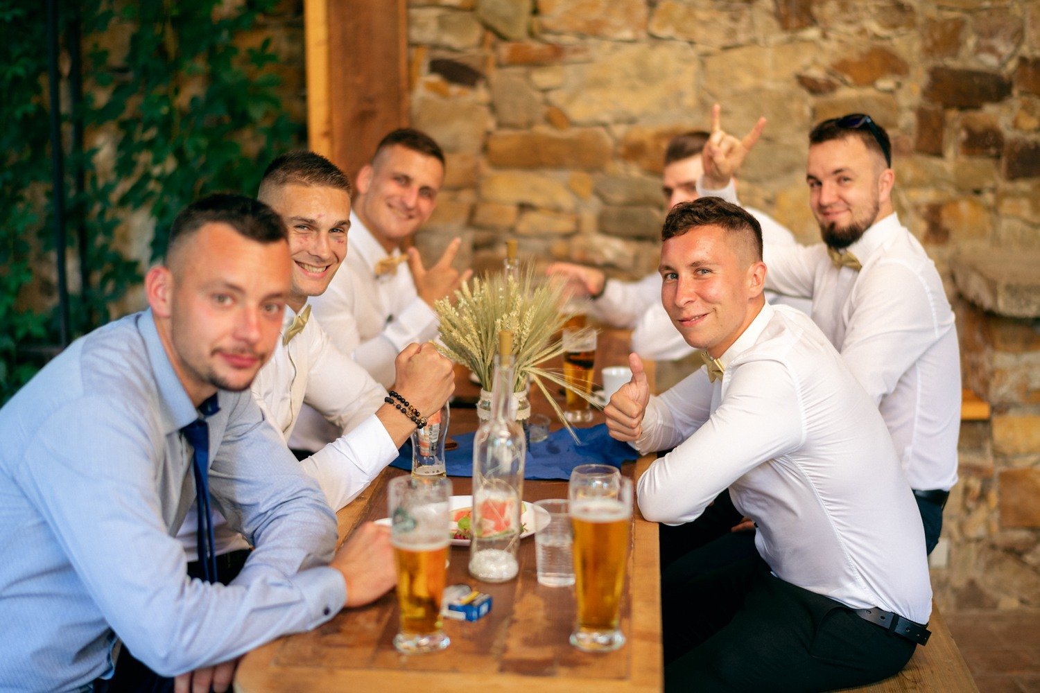 Skupina mužů připíjí pivem u kamenné stěny