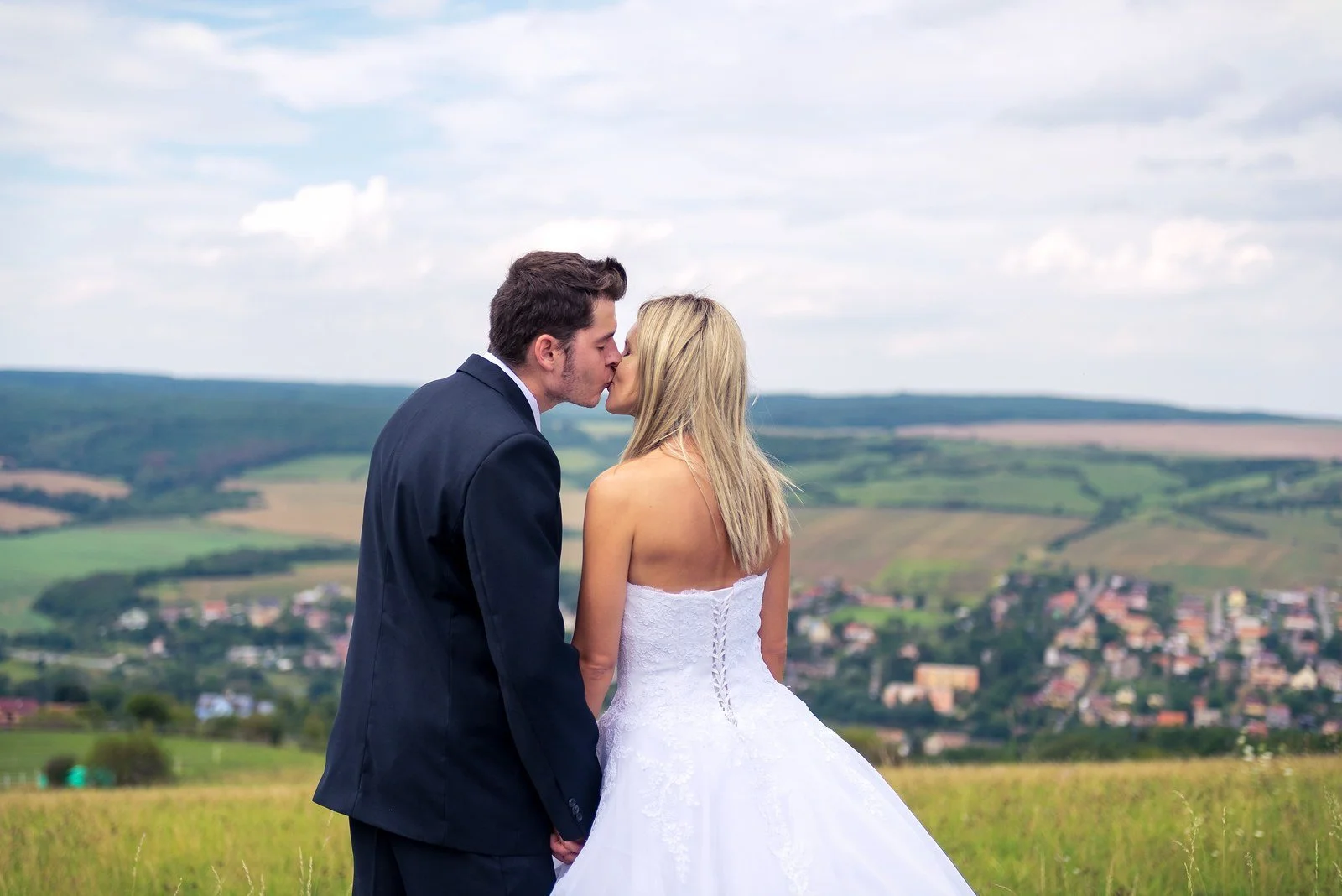 Petr a Ivana se líbají na vyhlídce nad městem a zalesněným údolím.