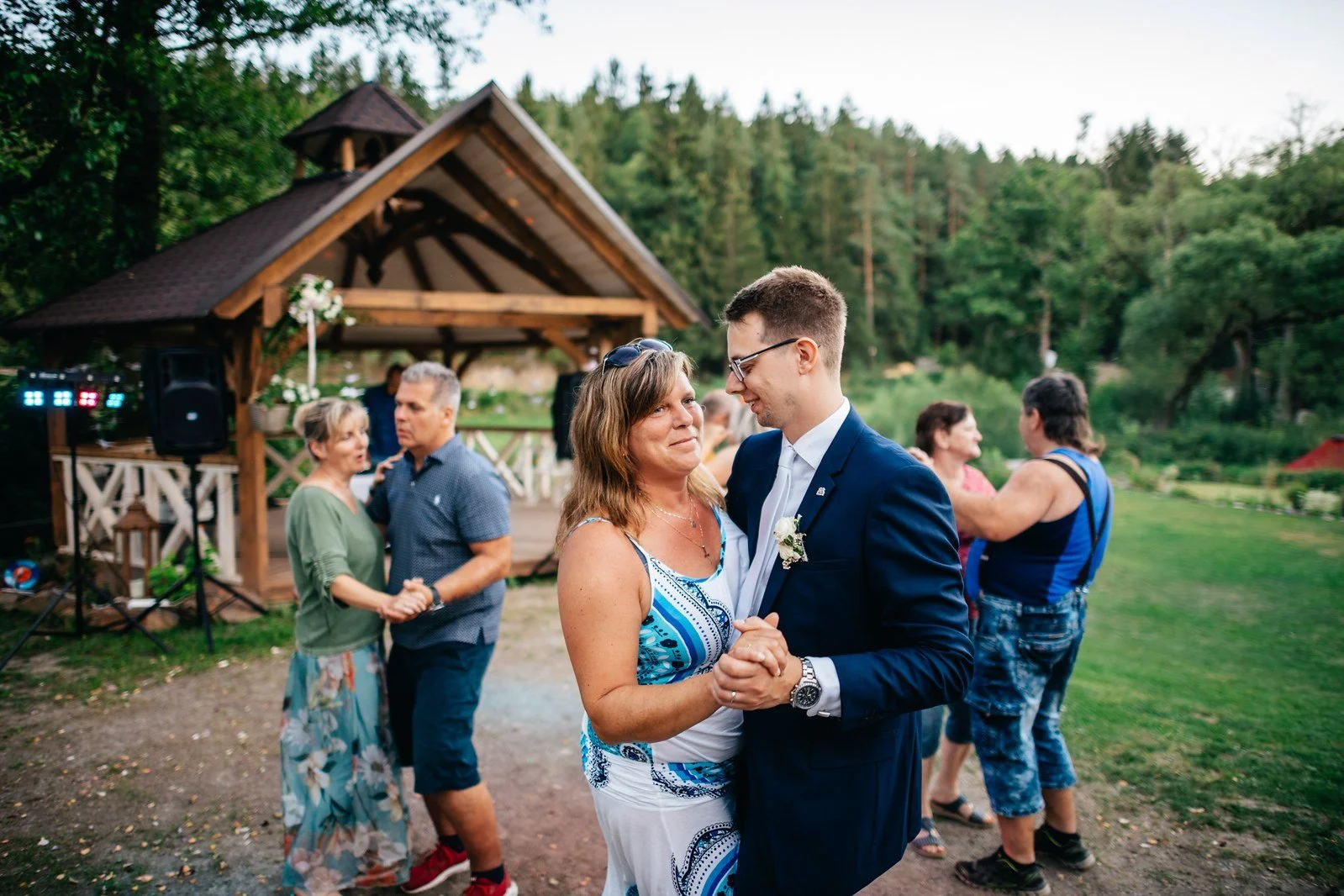 Ženich tančí se ženou v modrých šatech, zatímco kolem stojí další hosté.