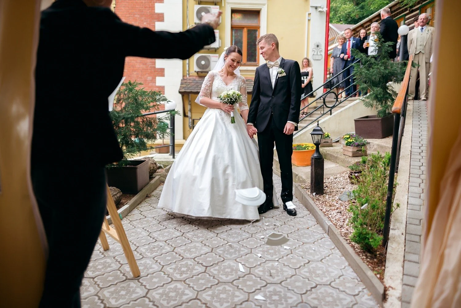Bílý talíř letí vzduchem před novomanželi stojícími na zahradní cestě.