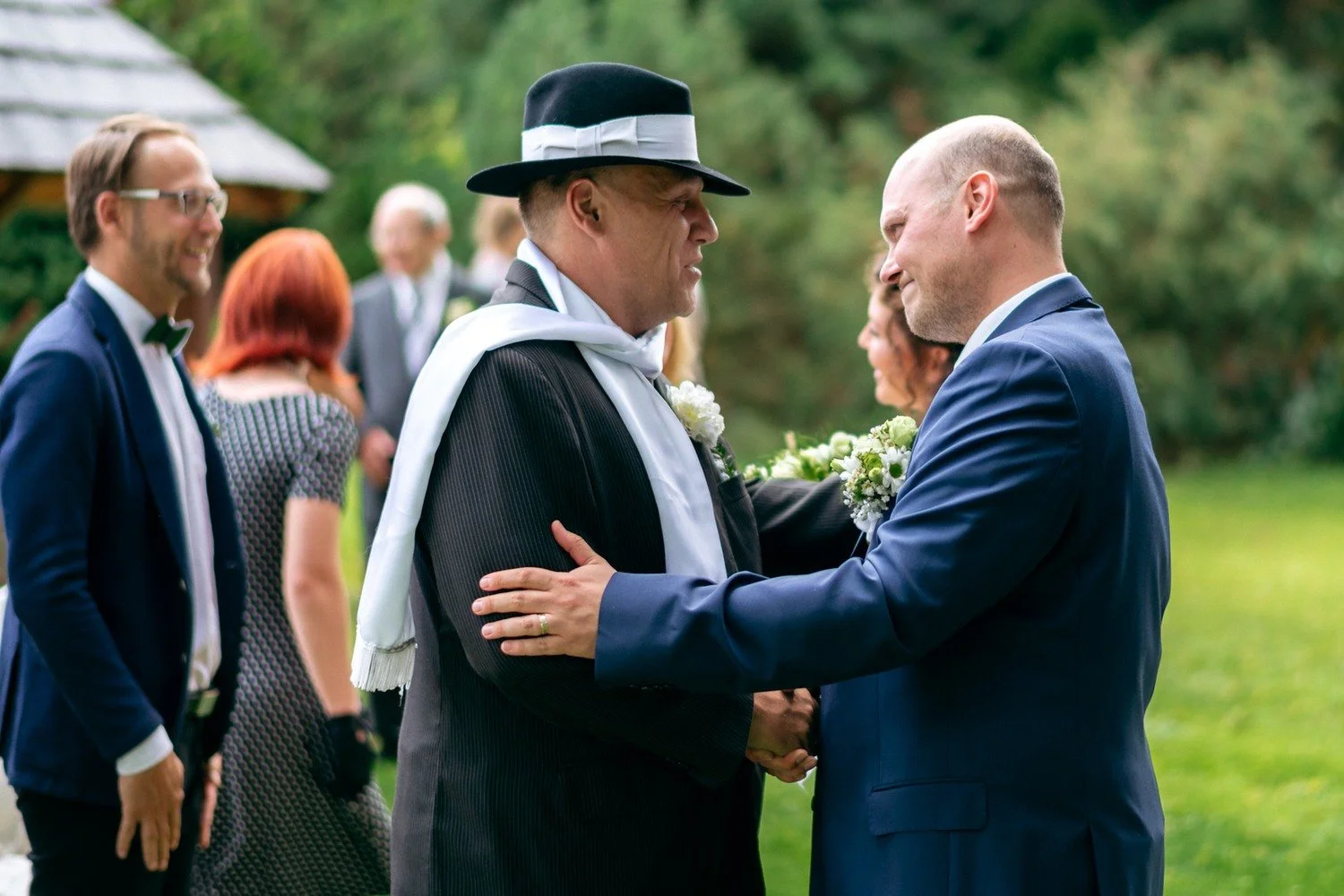 Ženich si podává ruku s mužem v černém klobouku.