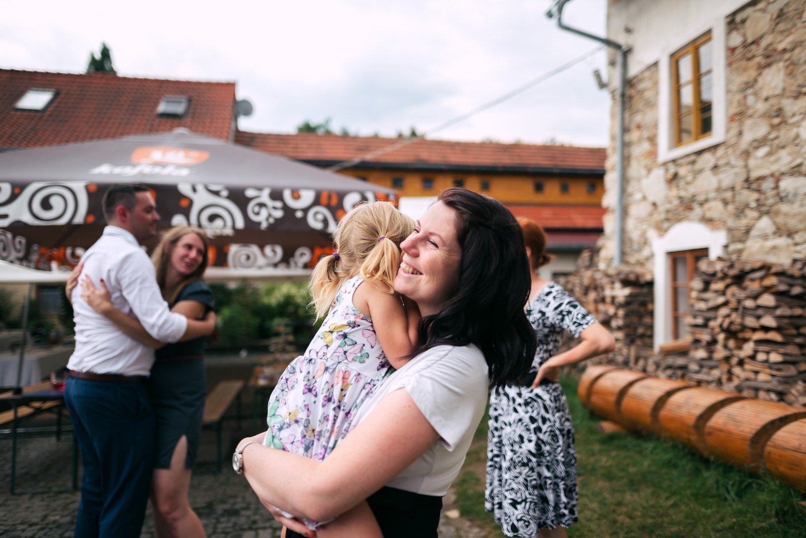 Dvě smějící se ženy se objímají u dřevěného zábradlí před kamennou budovou.