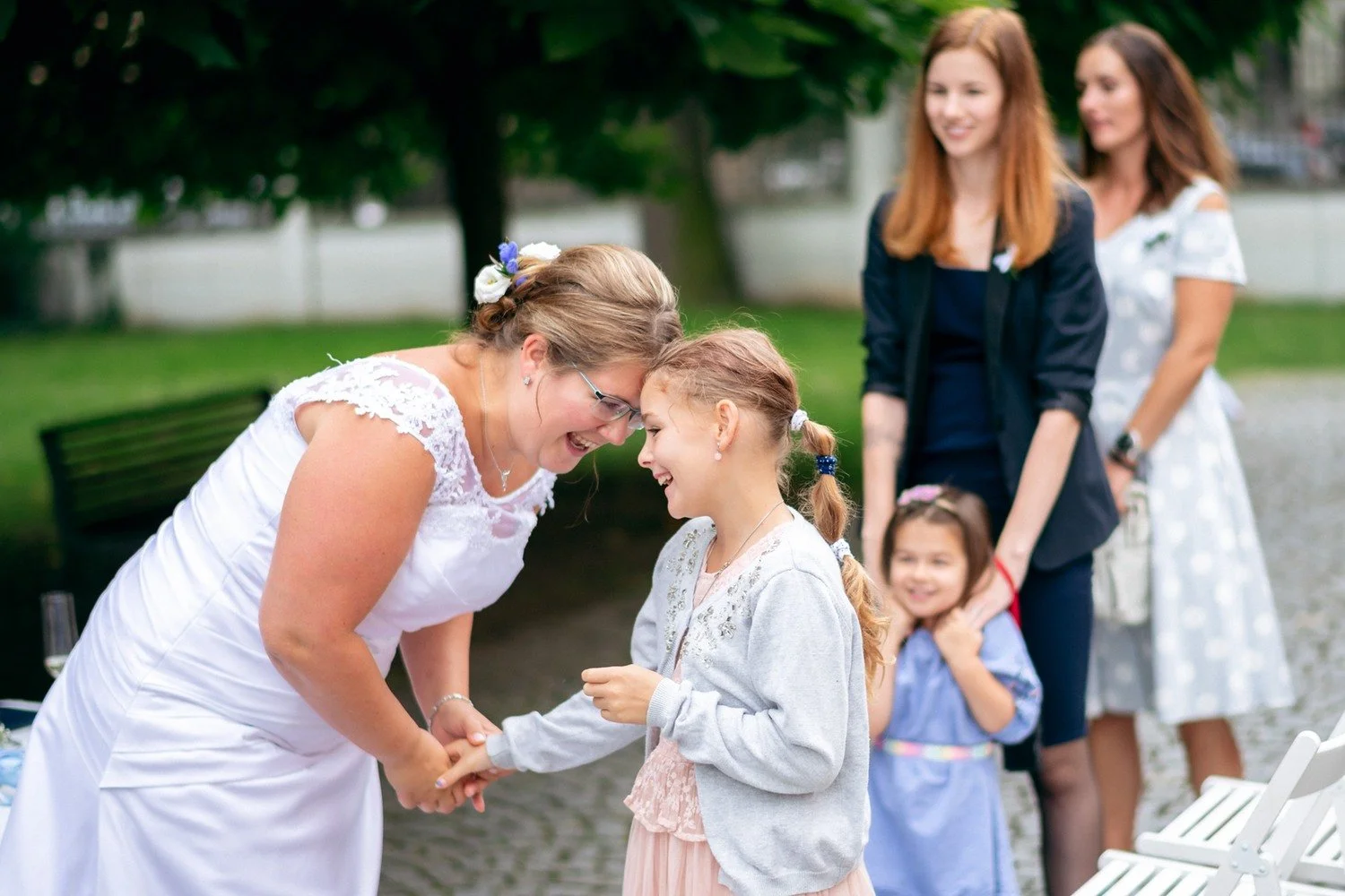 Nevěsta se sklání k dívce v zahradě, další děti stojí za nimi.