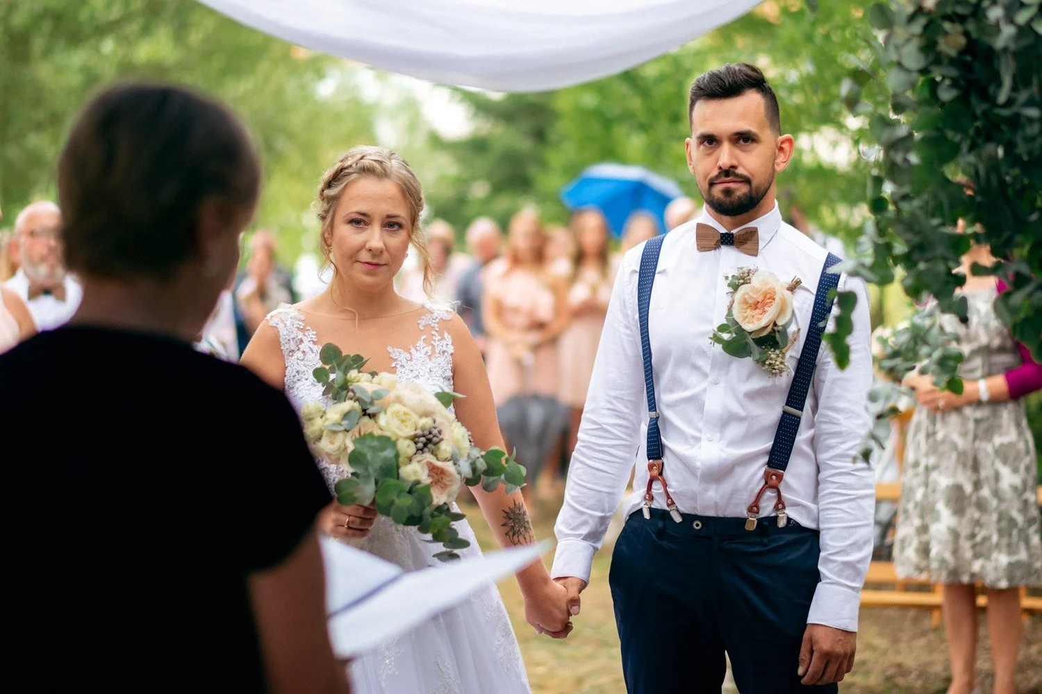 Nevěsta a ženich se drží za ruce během obřadu pod stromy.