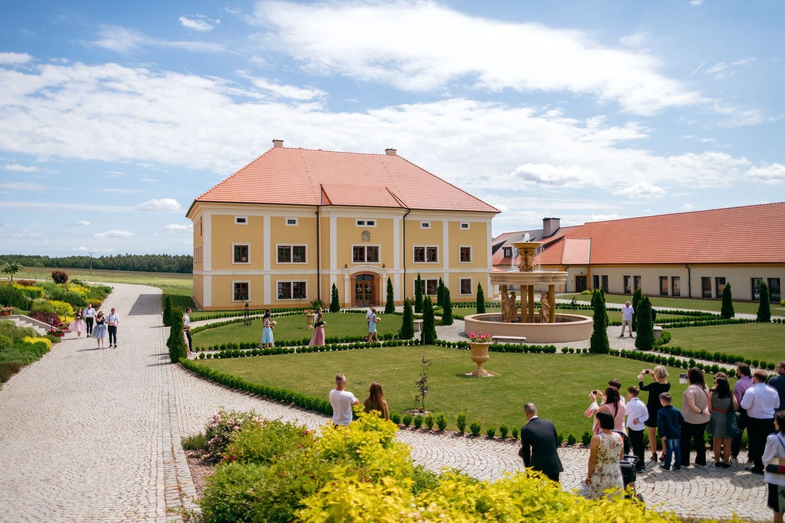 Řady bílých židlí čekají na hosty pod stromy u venkovního obřadu.
