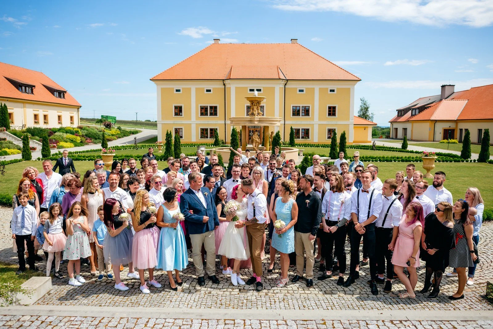 Hosté tleskají novomanželům na trávníku pod korunami stromů.