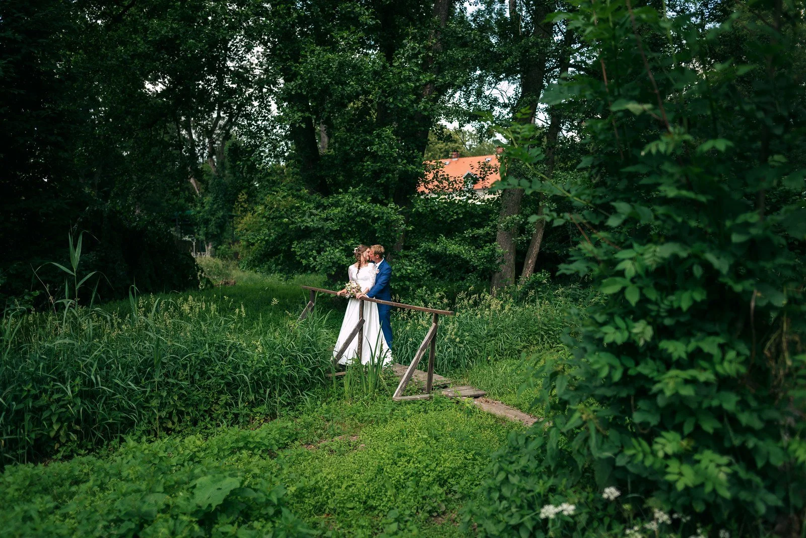Žena v bílých šatech stojí sama na lesní cestě.