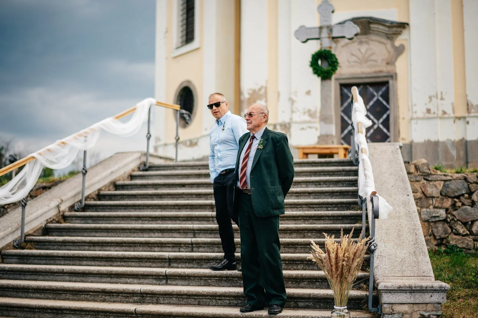 Muž stojí na schodišti kostela a očekává příchod ostatních.