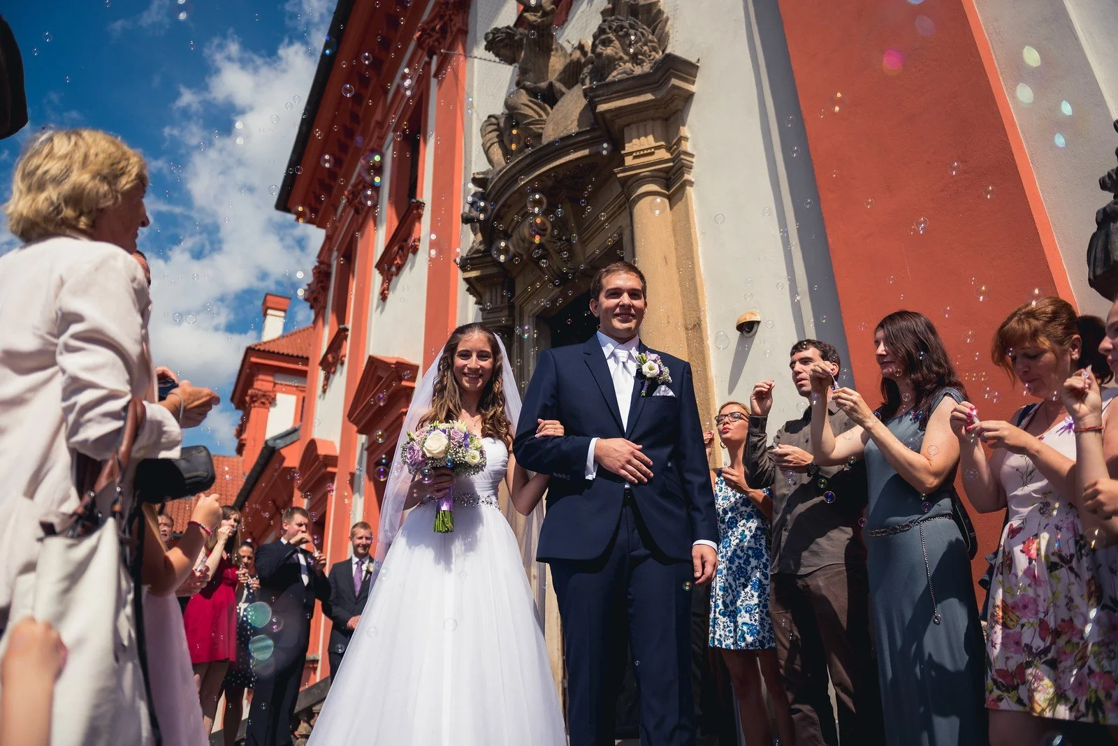 Dvojice vychází po schodech mezi lidmi a vířícími drobnými částicemi v jasném slunci.
