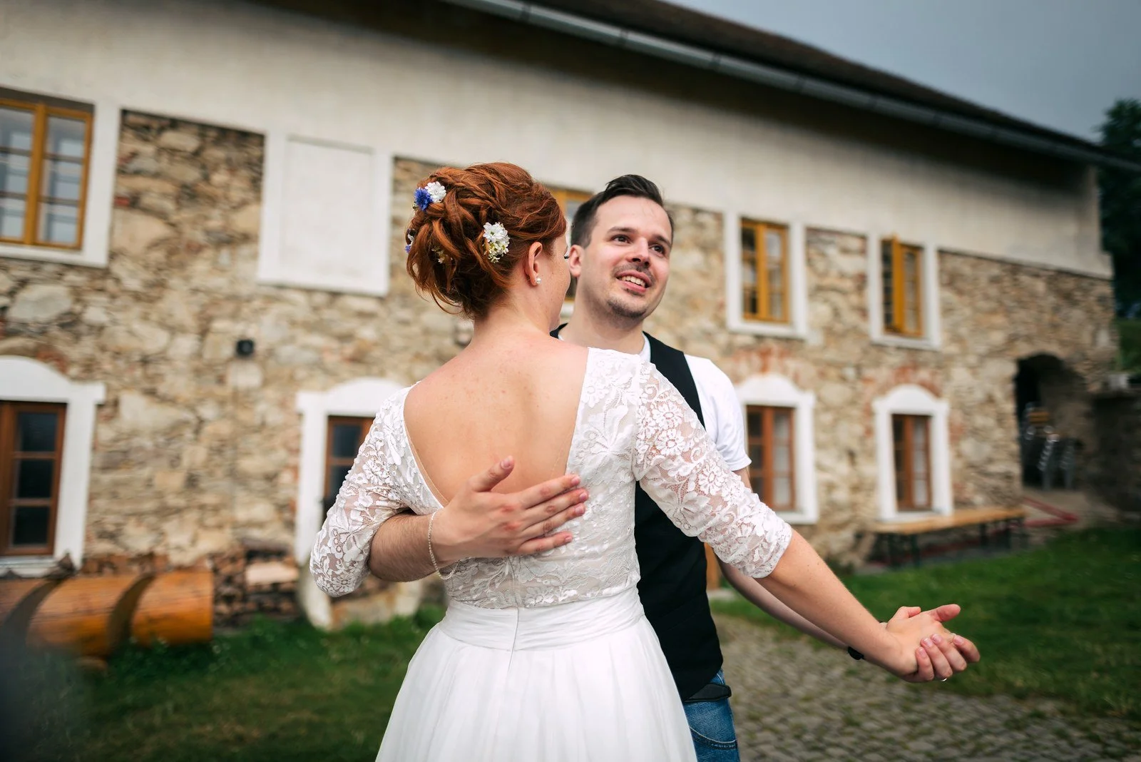 Tančící žena v bílých šatech rozpřahuje paže a muž za ní se směje.