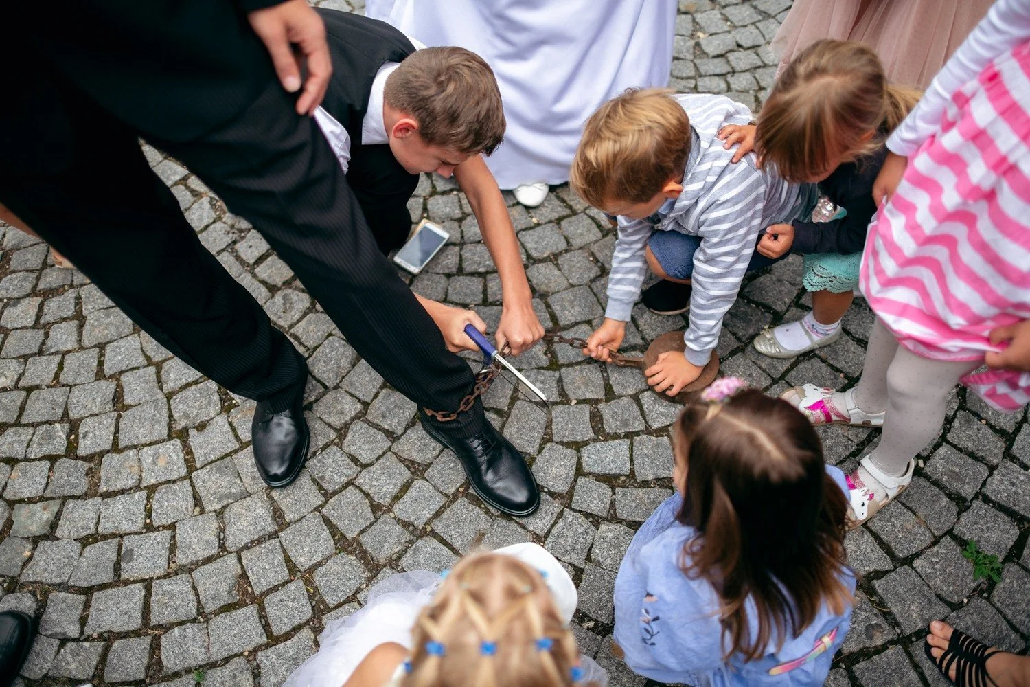 Pohled shora na děti a dospělé sklánějící se k předmětu na dlažbě.