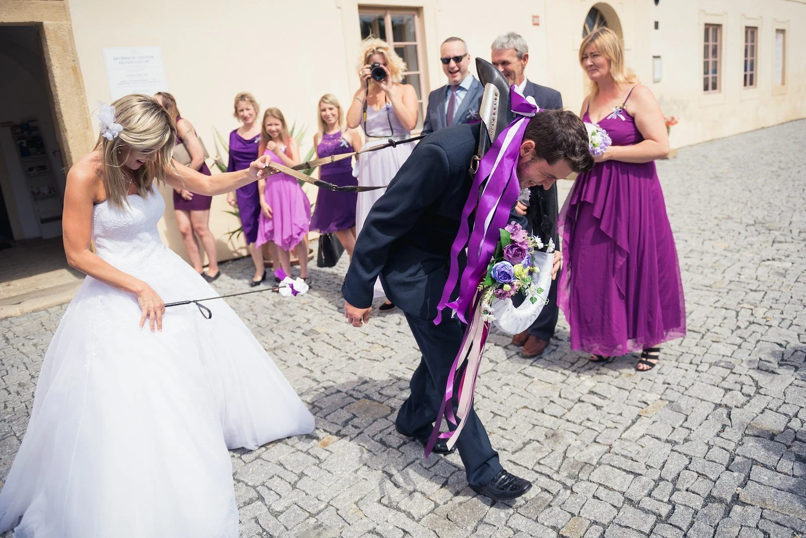 Petr se sklání pod fialovými stuhami, zatímco Ivana drží napnutou šňůru.