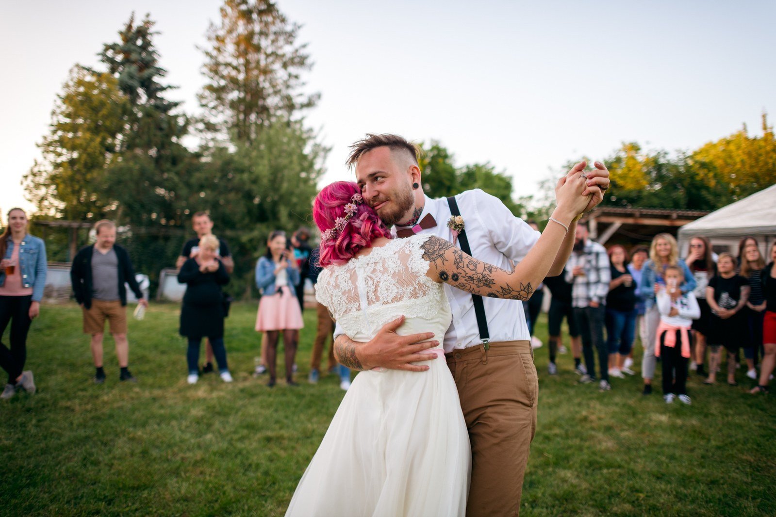 Skupina hostů se sklání kolem soutěžícího na trávníku před pergolou.
