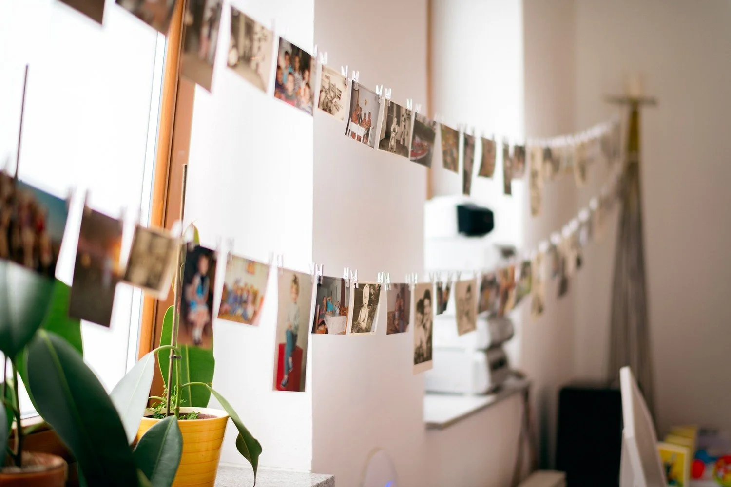 Dvě šňůry s připnutými fotografiemi vedou přes světlou stěnu kolem dřevěného kříže.