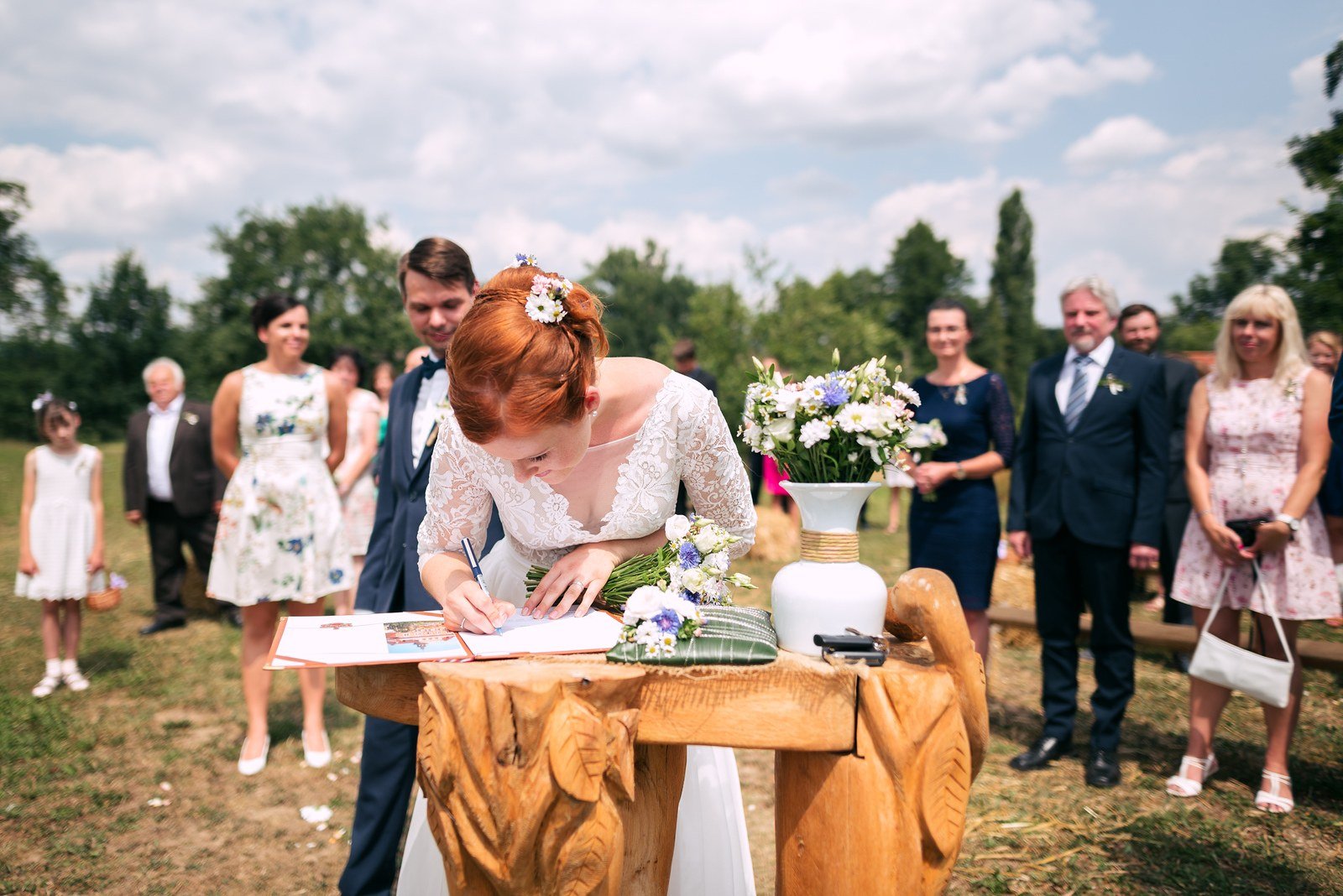 Žena se sklání nad dokumentem položeným na dřevěném stole s květinovou výzdobou.