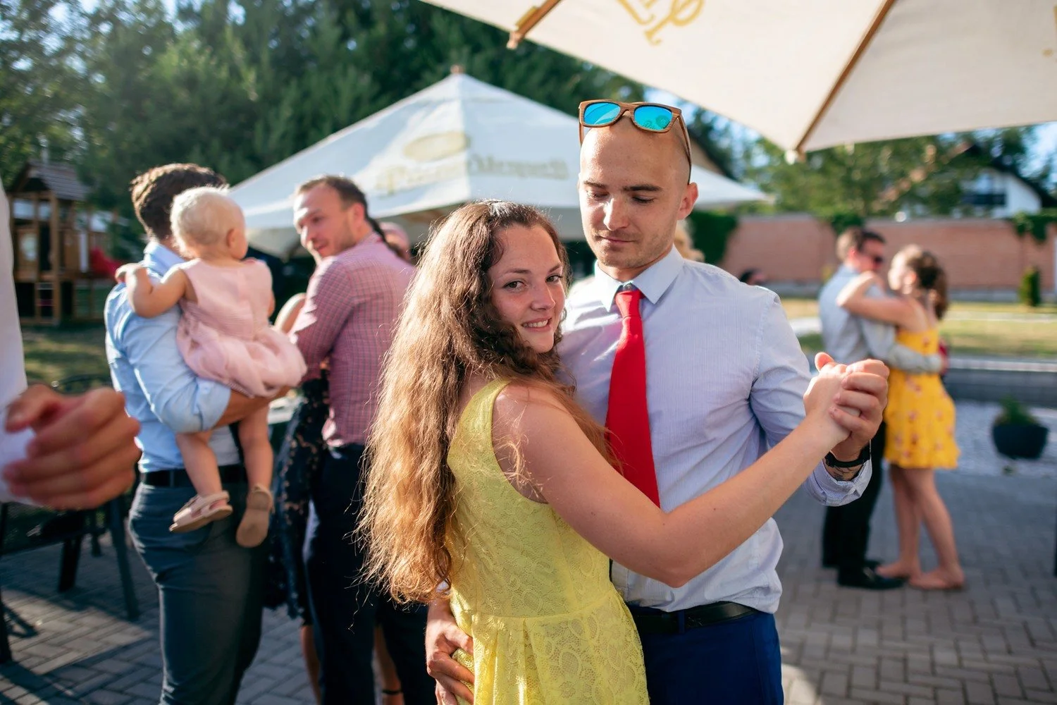 Žena ve žlutých šatech tančí s mužem v bílé košili a červené kravatě, který drží láhev.