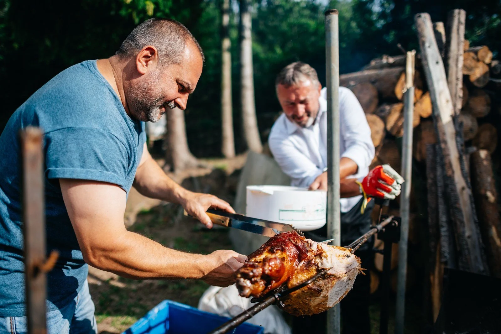 Muž u grilu pracuje nad pánví; ruce, jídlo a tmavé pozadí dávají záběru hmatatelnou energii.