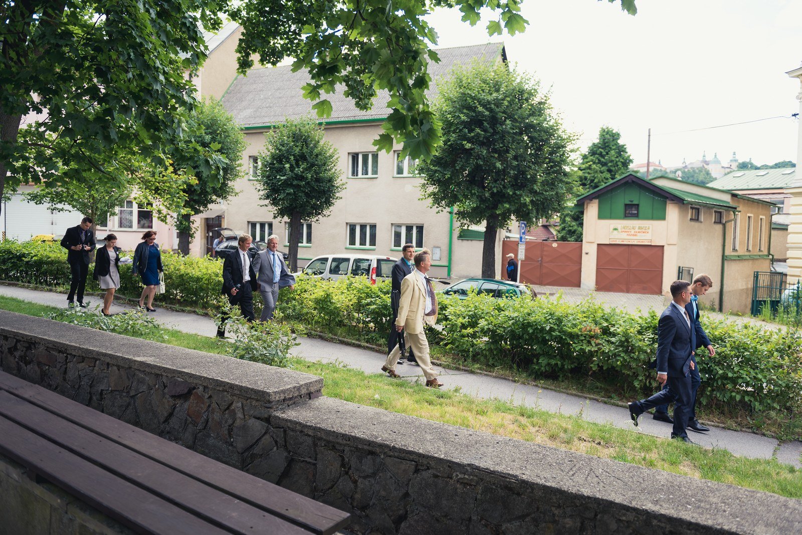 Svatební hosté přicházejí parkem k obřadní budově.