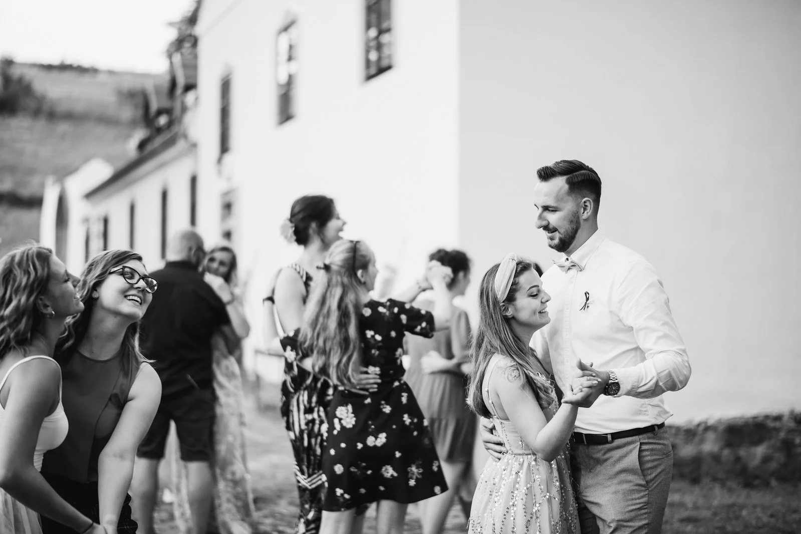 Skupina hostů se směje a povídá si před světlou budovou.