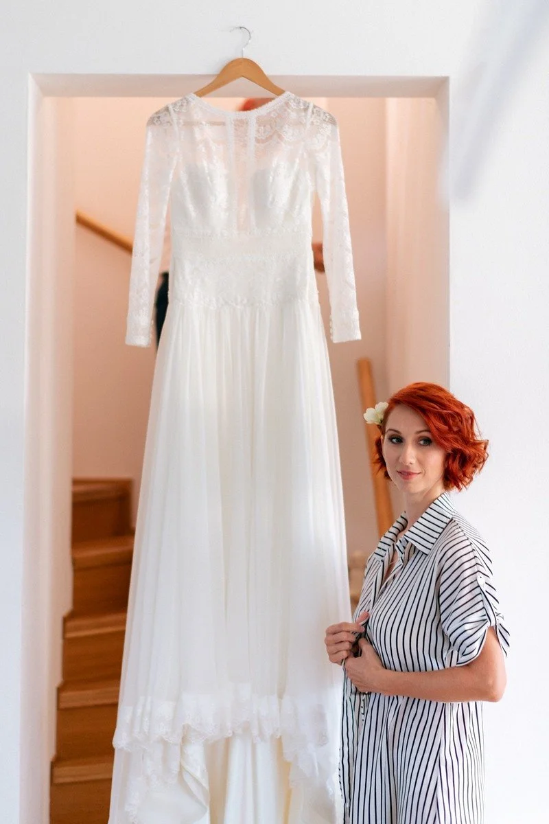 Martina stojí vedle zavěšených svatebních šatů.