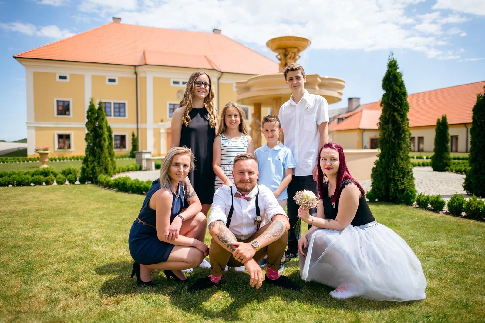 Novomanželé přijímají gratulaci od dvojice hostů pod stromy.