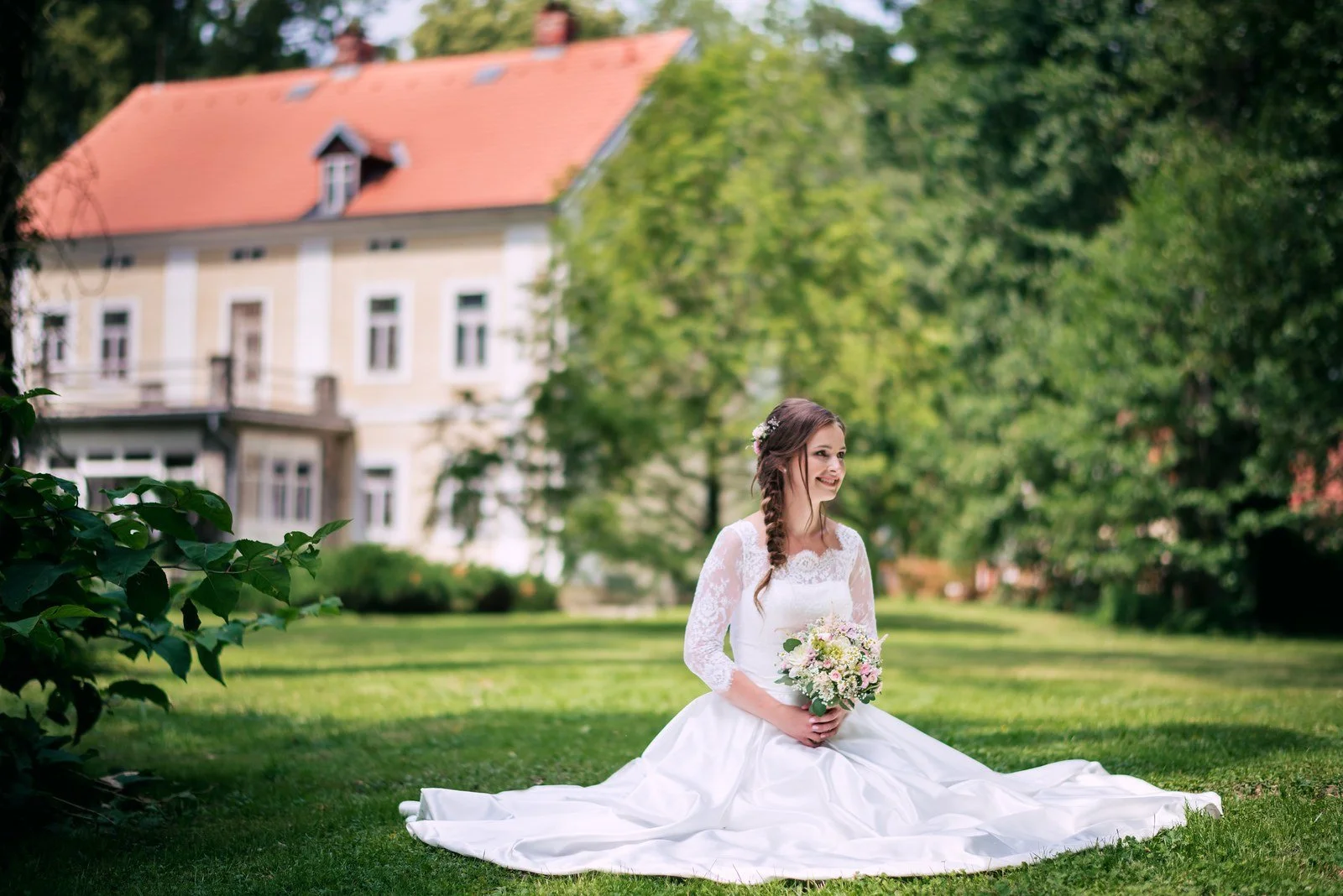 Žena v bílých šatech sedí na trávníku s rozprostřenou sukní.