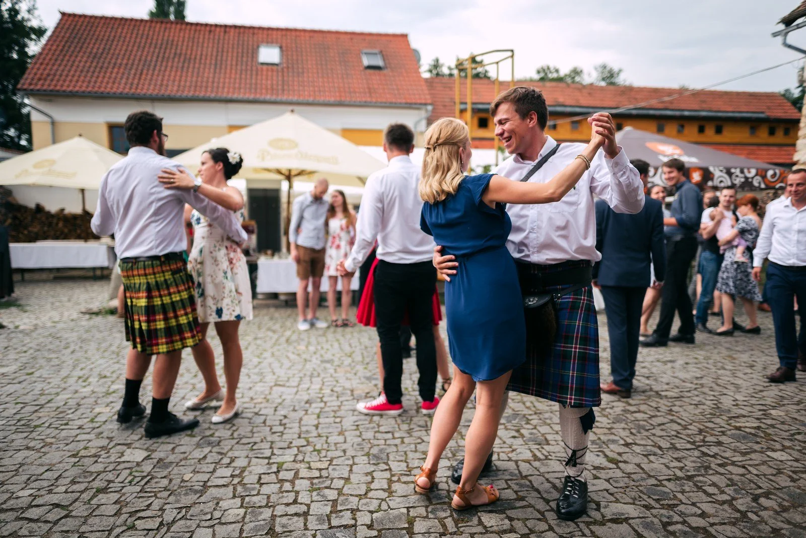 Několik žen tančí v řadě na nádvoří a drží se navzájem za ramena.