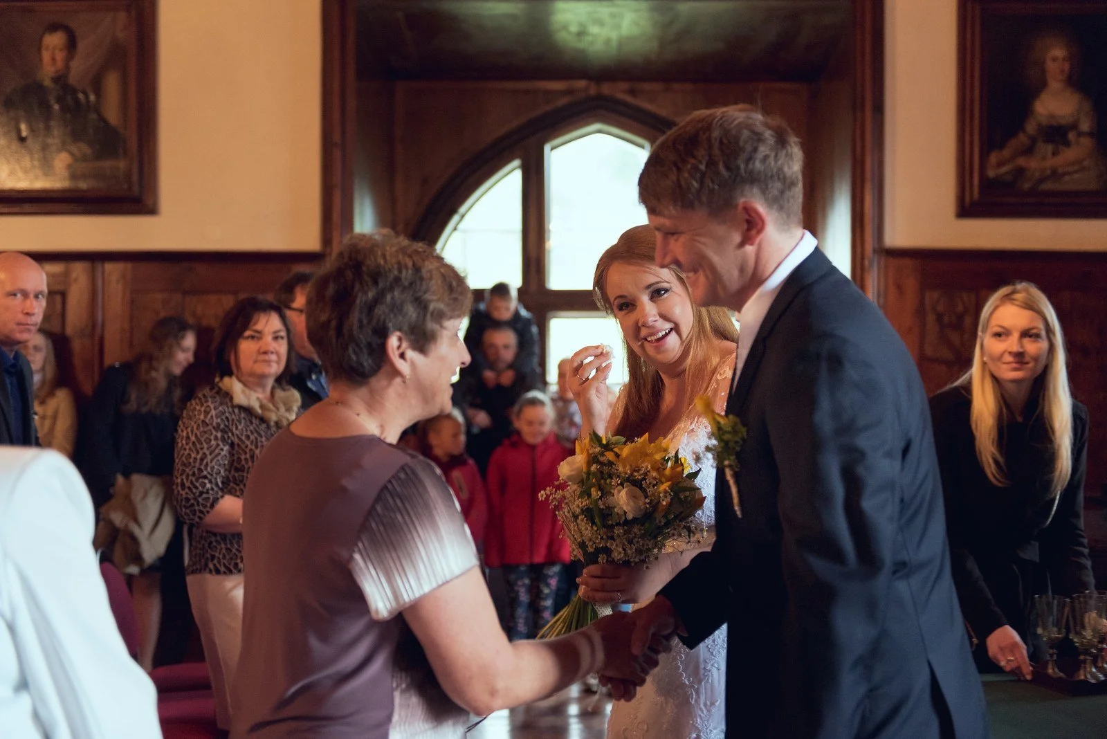 Ženich se naklání k hostu při gratulaci, nevěsta s kyticí stojí vedle.