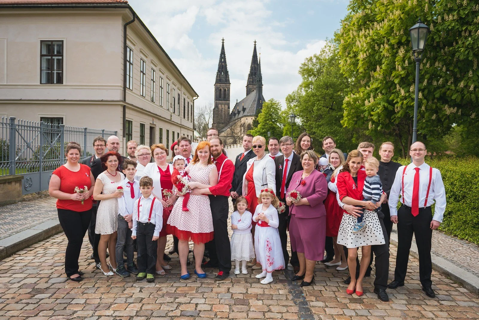 Velká skupina lidí pózuje na dlážděné cestě před kostelem.