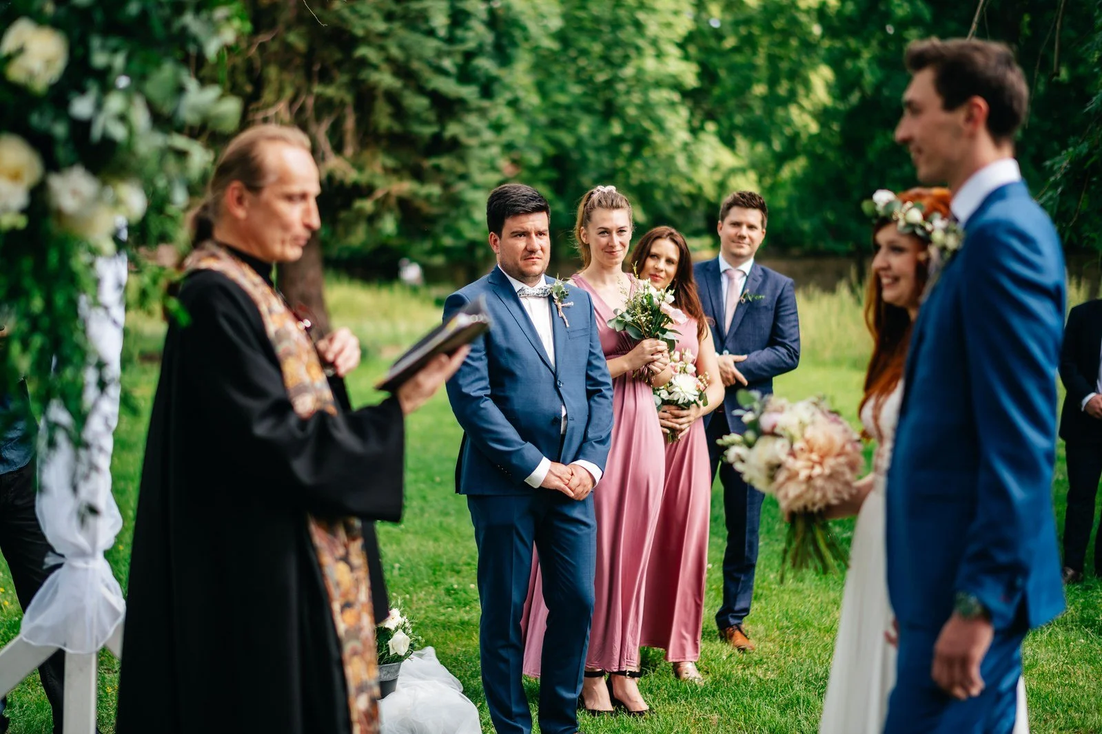Oddávající stojí před nevěstou a ženichem pod květinovým obloukem.