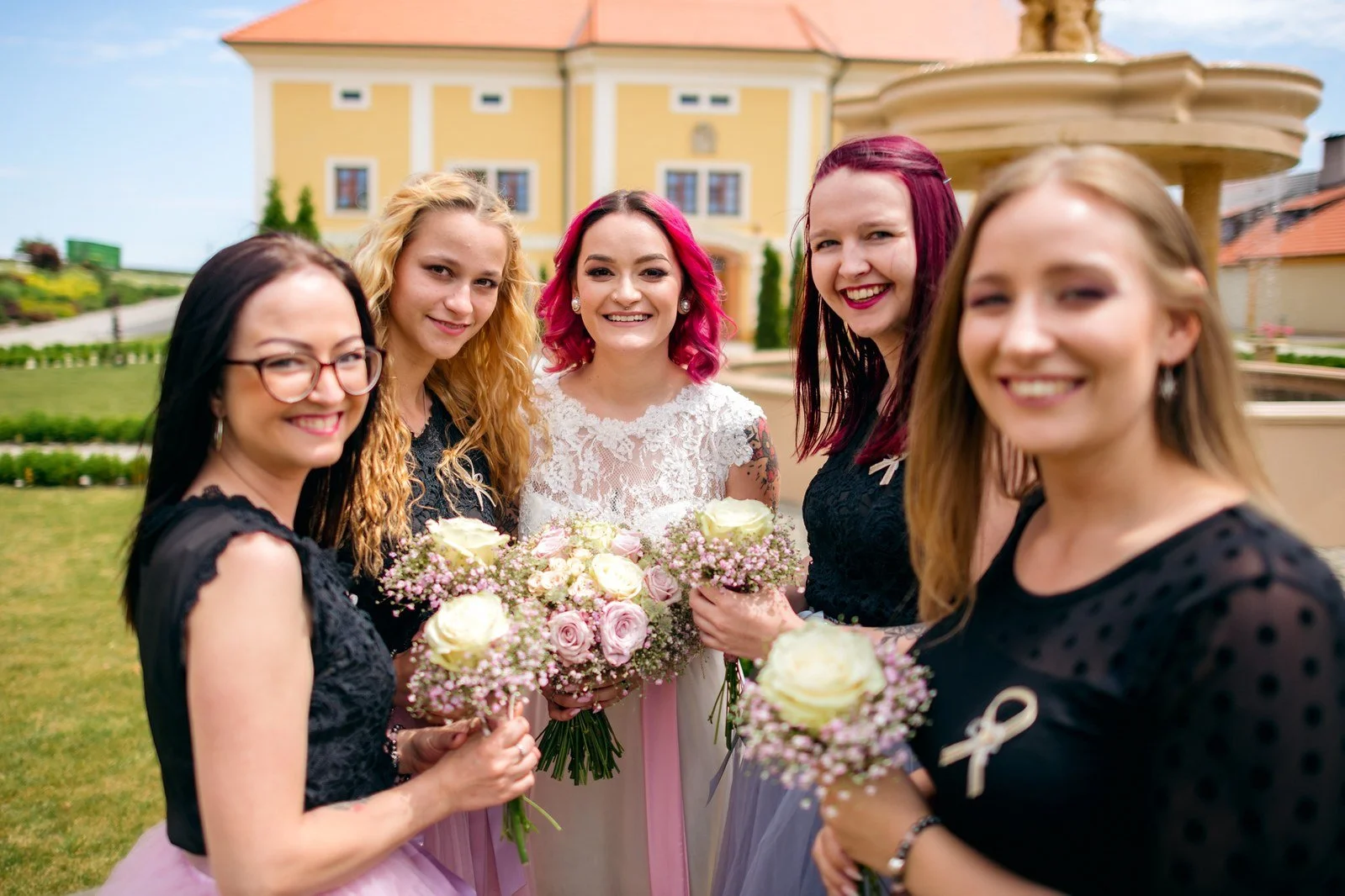Klára pózuje pod stromem se skupinou družiček v dlouhých růžových šatech.