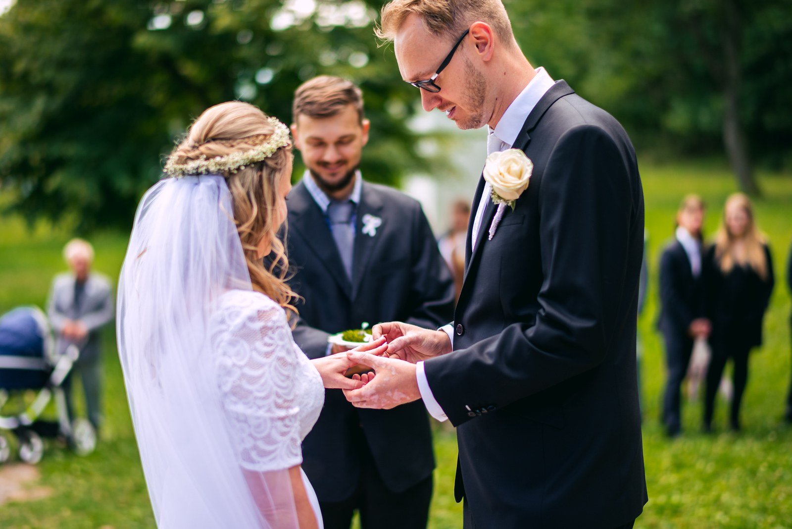 Skupina lidí vychází otevřenými dveřmi bílé budovy, uprostřed je žena v dlouhých bílých šatech.