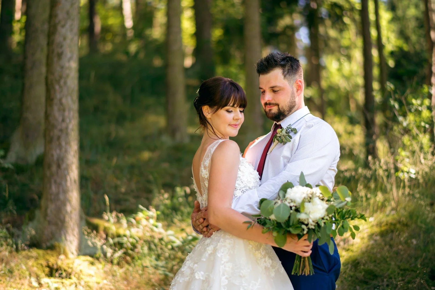 Radka a Pavel se objímají s kyticí v teplém světle mezi stromy.