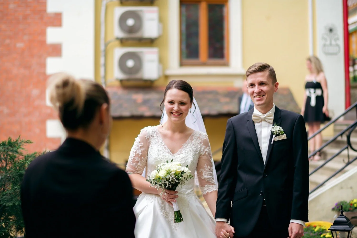 Usměvaví novomanželé přicházejí ruku v ruce k hostině.