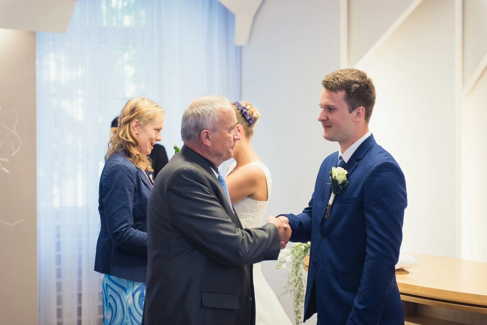 Starší host podává ženichovi ruku při gratulaci v obřadní síni.