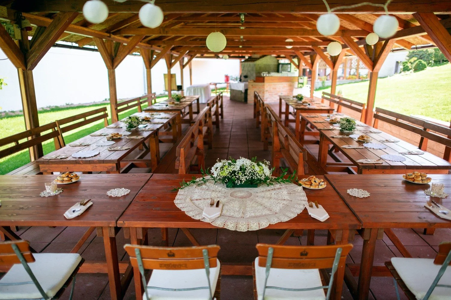 Dlouhé stoly jsou připravené v otevřeném dřevěném pavilonu.