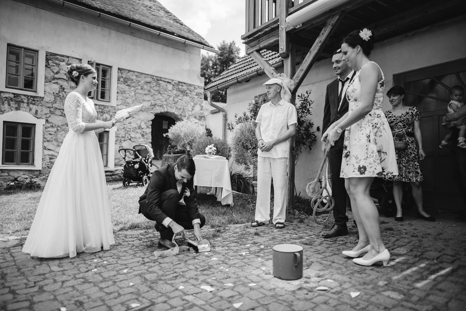 Černobílý snímek ukazuje dvojici na nádvoří, před níž klečí fotograf a kolem poletují bubliny.