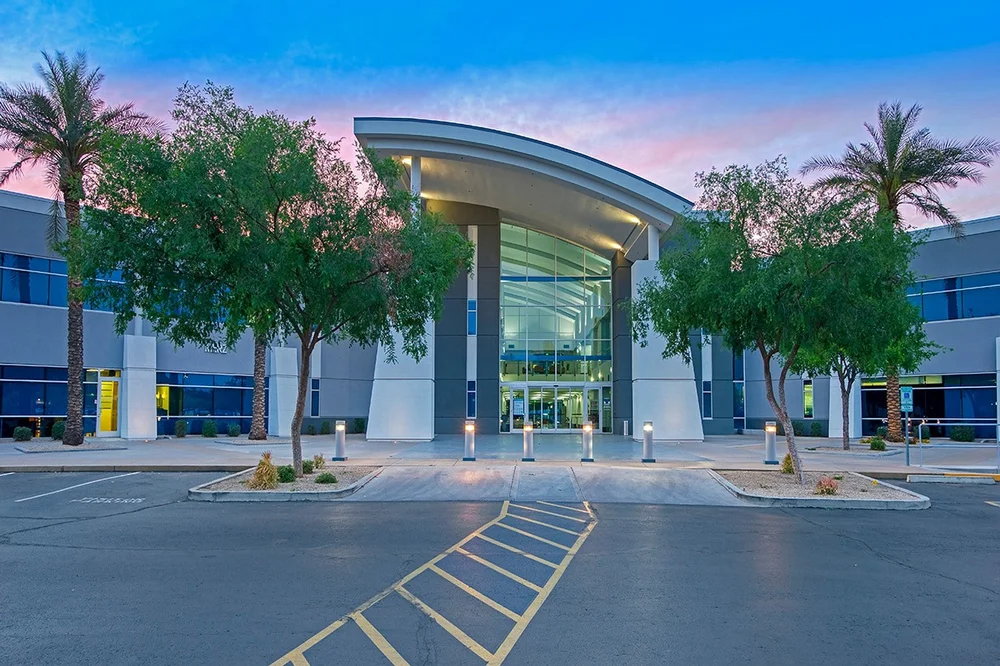 Medical office building entrance at 1840 South Stapley Drive, Mesa, at dusk, with a curved glass canopy over the entrance and palm trees flanking the walkway.