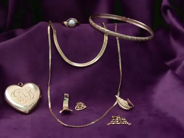 Gold chains, a gold bangle, an engraved heart locket, a pearl ring and small gold pieces on purple velvet