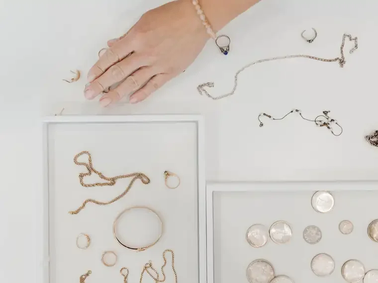 Gold jewellery and silver coins laid out on white trays