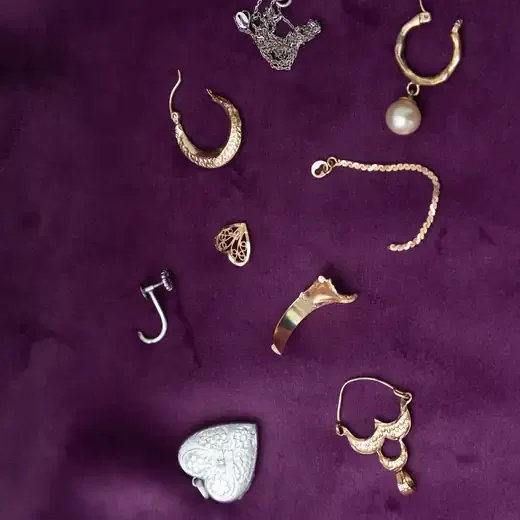 Single earrings, a broken chain and small pieces of gold and silver jewellery on purple velvet