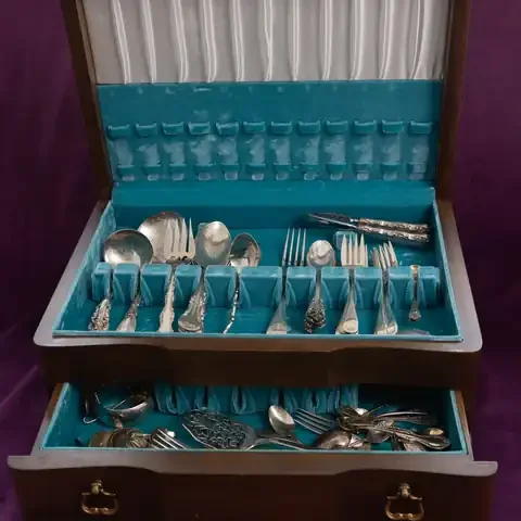 A wooden chest full of silver flatware on purple velvet