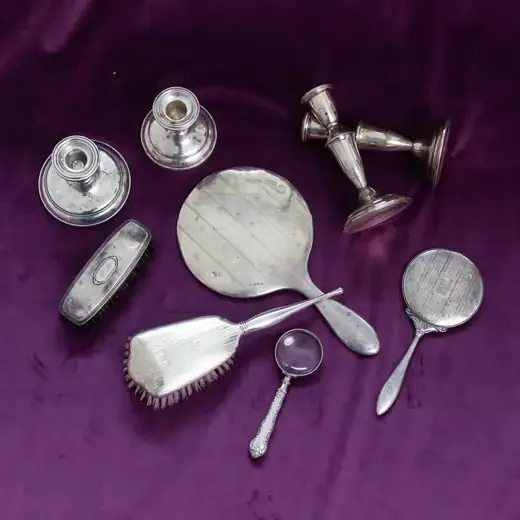 A sterling silver hand mirror, brush, candlesticks and small vanity pieces on purple velvet