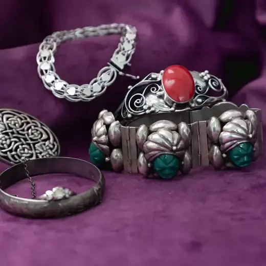 Sterling silver bracelets, a cuff with a red stone and a Celtic brooch on purple velvet