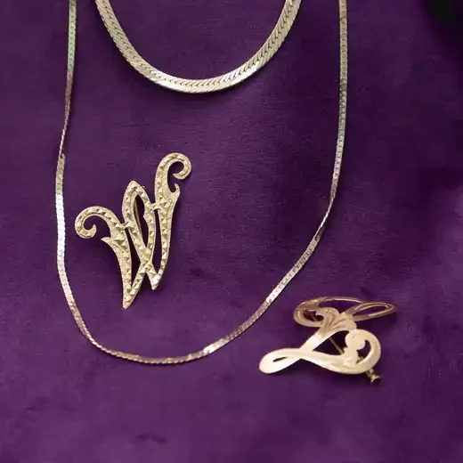 Gold herringbone chains and two gold letter brooches on purple velvet